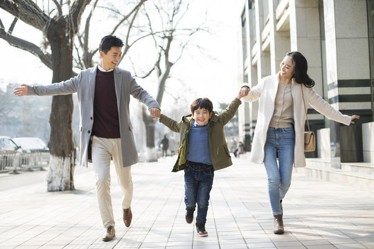 Cheerful young Chinese family holding hands running