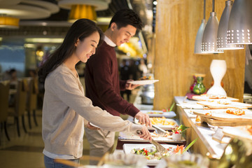 Cheerful young Chinese couple taking food from buffet table