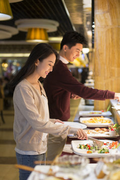 Cheerful young Chinese couple taking food from buffet table