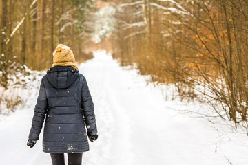 Warm dressed woman in winter, walking on snow path in park, girl in black coat, back view