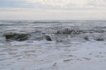 Foaming waves crashing on ocean beach with cloudy sky