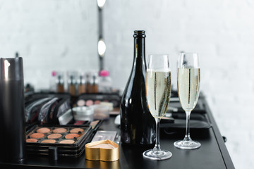 close up view of bottle and glasses of champagne on tabletop with cosmetics for makeup