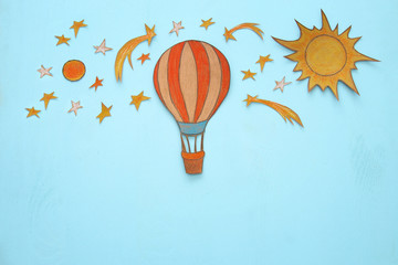 Hot air balloon, space elements shapes cut from paper and painted over wooden blue background.