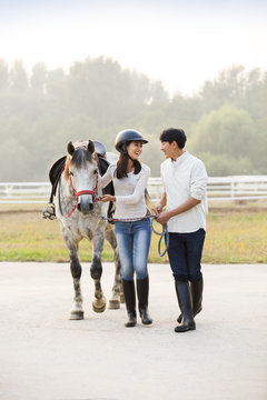 Cheerful young Chinese couple walking with horse 