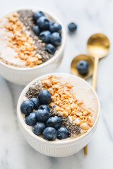 Smoothie bowls with fresh ripe blueberry, nuts, chia, banana and soya milk over white marble. The concept of healthy eating and vegetarian food.