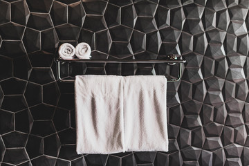 Four clean white towels on holder in hotel bathroom with textured black wall. Modern minimal style