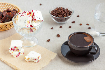 A cup of black coffee and a few pieces of homemade nougat with peanuts and dried cranberries
