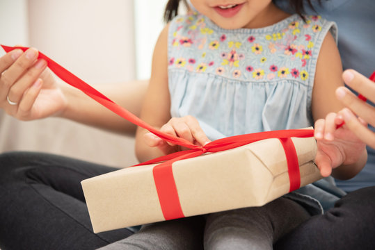 Child Daughter Unwrapping Gift Box With Her Mom.