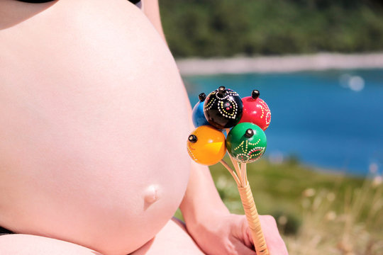 Pregnant Woman Is Holding Classic Colorful Rattle Baby Bell Toy On Pregnant Belly. Future Mom And Parent Is Waiting Baby, Love And Happiness. Birth Expectation Concept. Pregnancy, Abdomen, Motherhood.