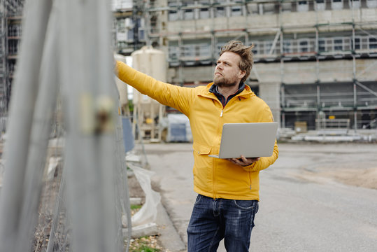 Man holding laptop, construction site in the background