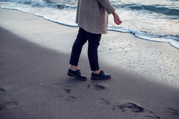 Woman in coat and trousers walking by seashore with flying seagulls
