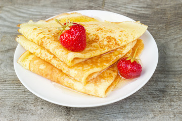 Tasty sweet thin pancakes with fresh strawberries and honey on plate, delicious dessert, closeup, wooden background