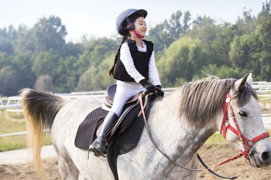 Cheerful little Chinese girl riding horse 