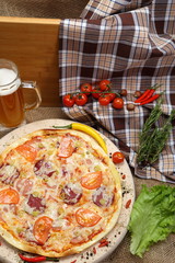 Pizza with tomato, cheese, smoked sausage, boiled sausage, pepper spices on a wooden tray, with beer in a glass mug close-up