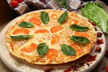 Pizza with tomato, cheese, salad, on a wooden stand closeup