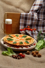 Pizza with beer in a glass mug with tomato, cheese, salad, on a wooden stand closeup