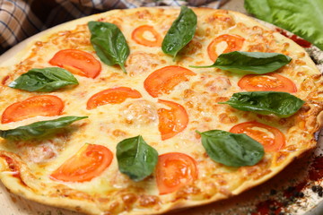 Pizza with tomato, cheese, salad, on a wooden stand closeup