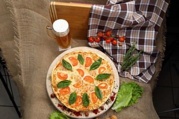 Pizza with beer in a glass mug with tomato, cheese, salad, on a wooden stand closeup