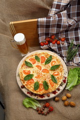 Pizza with beer in a glass mug with tomato, cheese, salad, on a wooden stand closeup