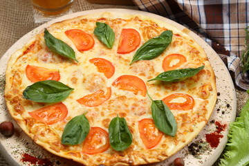 Pizza with beer in a glass mug with tomato, cheese, salad, on a wooden stand closeup