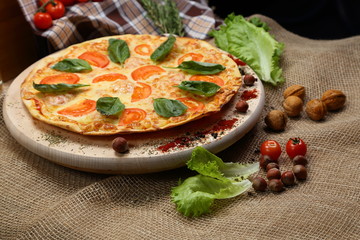 Pizza with tomato, cheese, salad, on a wooden stand closeup