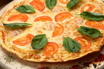 Pizza with tomato, cheese, salad, on a wooden stand closeup