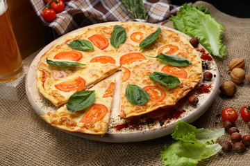 Pizza with tomato, cheese, salad, on a wooden stand closeup