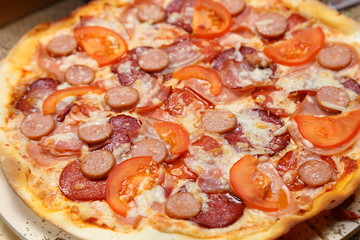 Pizza with sausages, tomato, smoked sausage, bacon, red pepper and cheese close-up
