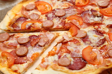 Pizza with sausages, tomato, smoked sausage, bacon, red pepper and cheese close-up