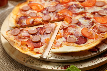 Pizza with sausages, tomato, smoked sausage, bacon, red pepper and cheese close-up