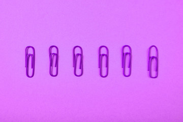 Violet paper clips isolated on violet background, close up, copy space. Top view, flat lay. Back to school, college, education concept