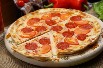 Pizza thin with smoked sausage, cheese, spices and tomatoes on a wooden stand. Cherry tomatoes and sweet peppers, lettuce leaves. Close-up
