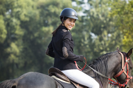 Cheerful young Chinese woman riding horse 