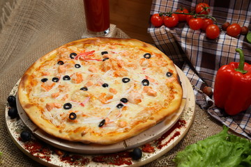 pizza thin olives, shrimps, crabs, seafood, on a wooden stand with tomato juice in a glass sink. Cherry tomatoes and sweet peppers, lettuce leaves. Close-up