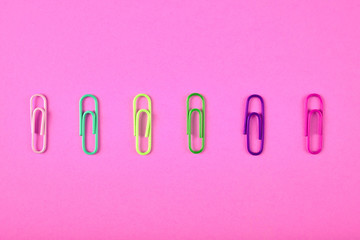 Colorful paper clips isolated on pink background, close up, copy space. Top view, flat lay. Back to school, college, education concept. White, tuqruois, yellow, green, violet, pink paperclips