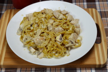 Macaroni with chicken meat and mushrooms. Spice. Red metal glass with a spoon, fork and knife.