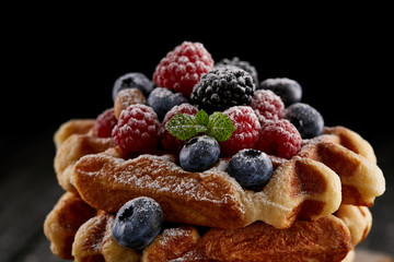 close-up shot of delicious belgian waffles with berries spilled with sugar powder on black