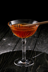 close-up shot of glass of honey with wooden spoon on black wooden table