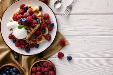 top view of freshly baked belgian waffles with berries and ice cream on white wooden table