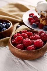 close-up shot of bowls with berries with belgian waffles blurred on background on white wooden table