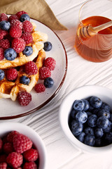 close-up shot of delicious belgian waffles with berries and honey on white wooden table