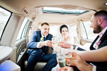 Groomsmen with bridesmaids and wedding couple drinking champagne in the car.