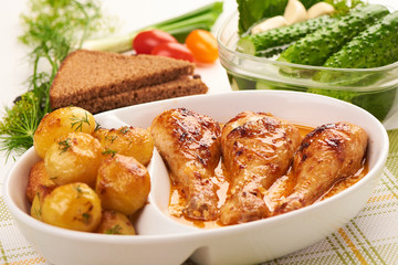Appetizing baked chicken legs with cream sauce, potatoes and spices on white background.