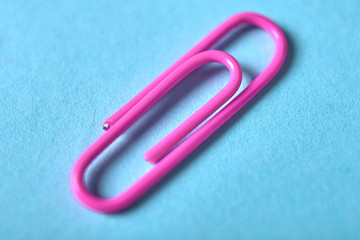 One violet paper clip isolated on blue background, close up, copy space. Top view, flat lay. Back to school, college, education concept