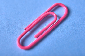 One pink paper clip isolated on blue background, close up, copy space. Top view, flat lay. Back to school, college, education concept