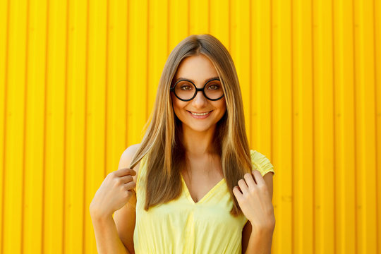 Beautiful young woman in funny toy glasses smiling over yellow background at daylight