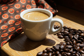 Cup of espresso in white cup with coffee beans on wooden background