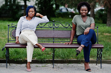 Two african girls posed at street of city sitting on the bench.