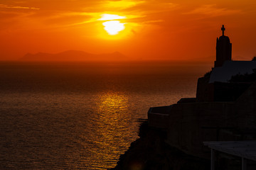 Beautiful sunset with silhouette of chapel on the cliff in Oia Santorini Greece