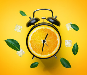 Alarm Clock of Orange Fruit Green Leaves and Ice Cube Flying Around on Yellow Background. Summer...